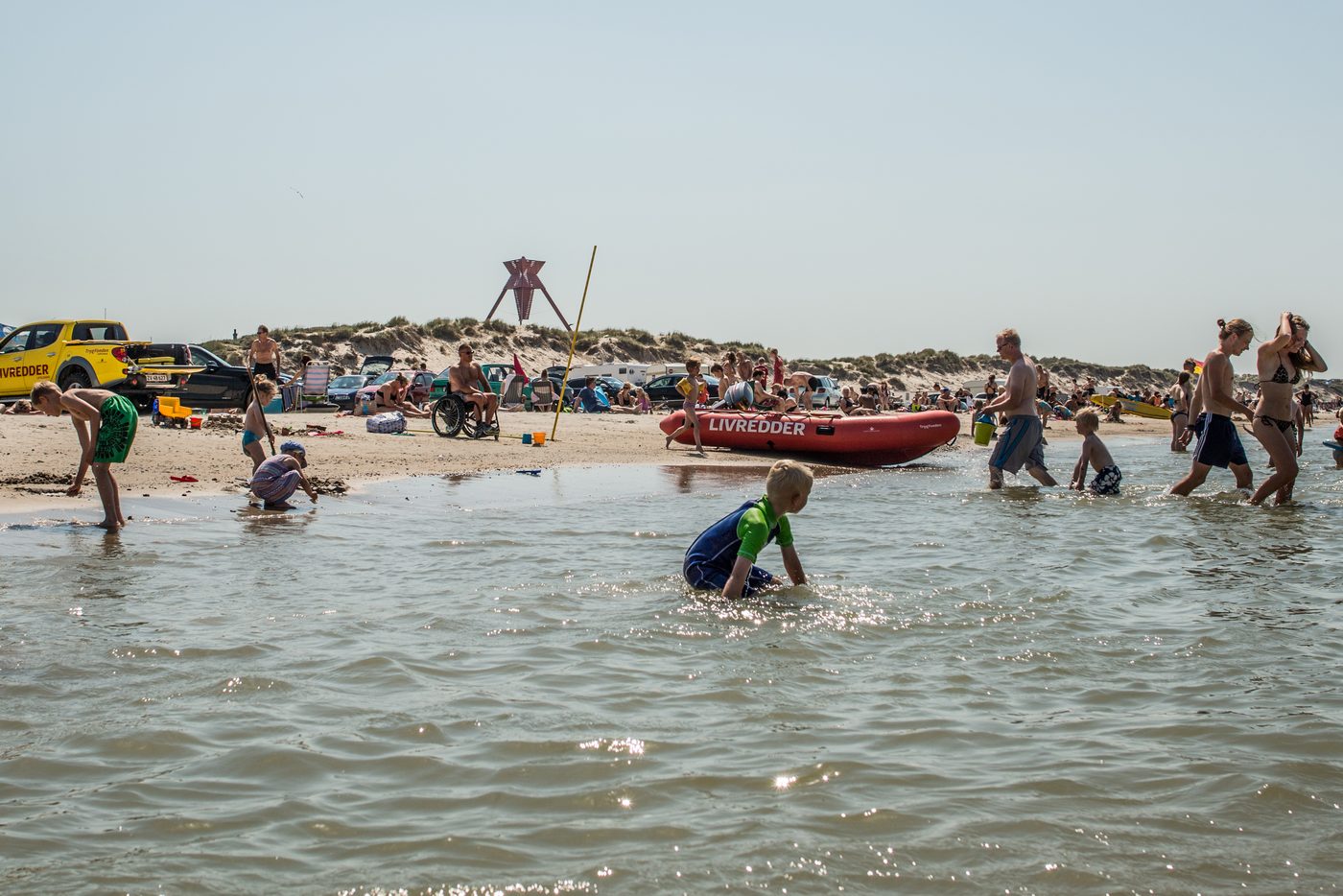 Hvide Sande beach in summer — families in the water, lifeguard boat marked LIVREDDER on the shore