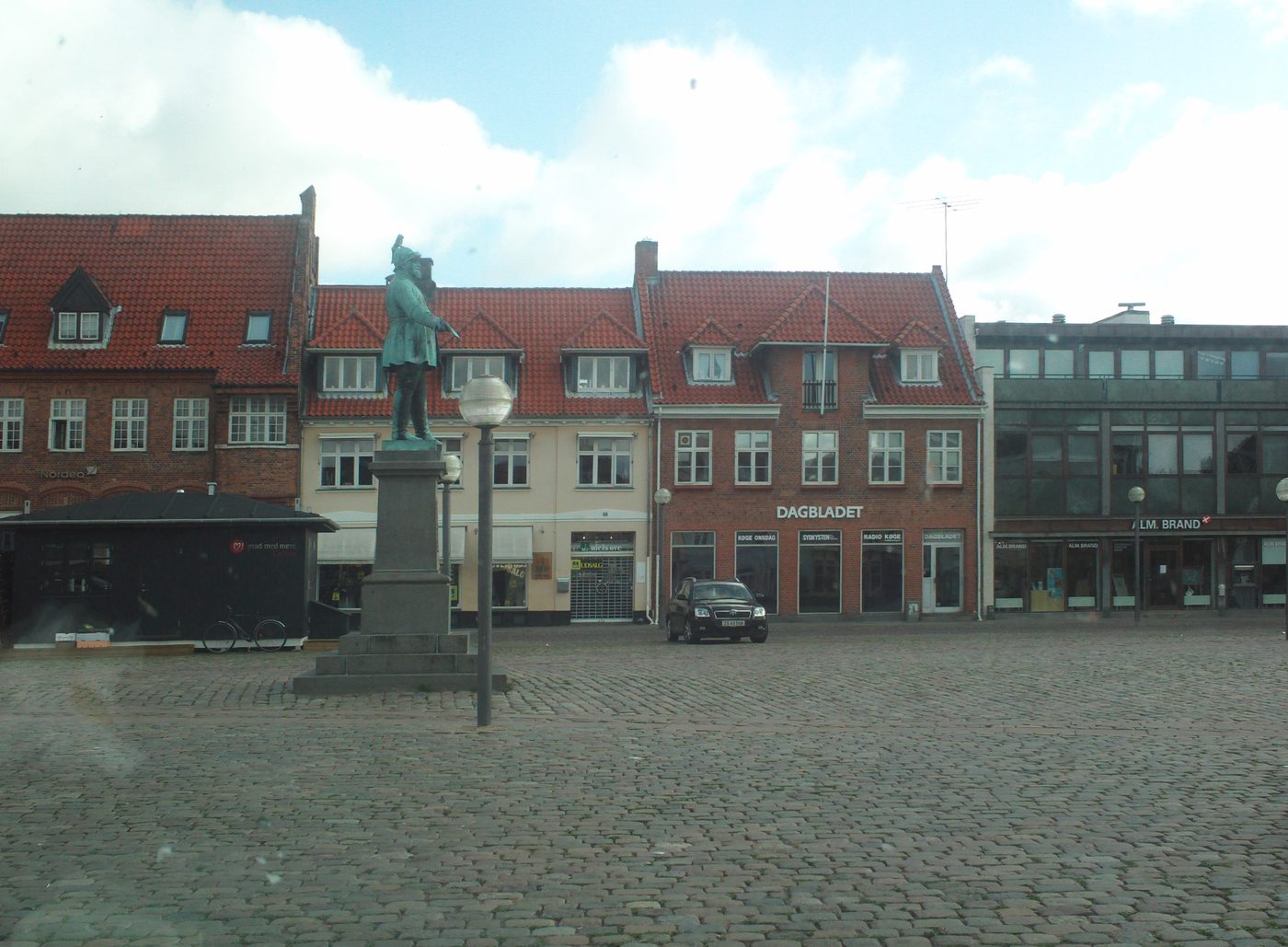 Køge town square at midday — the kind of café-lined plaza eight minutes' walk from the Supercharger