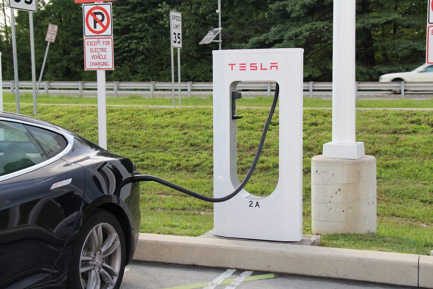 Tesla connected to a Supercharger stall, charge port lit, cable in place